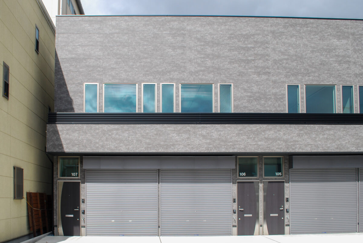 東大阪市高井田中に建つ木造2階建ての駐車場付きテナント事務所ビル外観。外壁にKMEWフィエルテを採用し、倉庫と事務所を併設した施工事例。