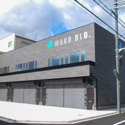 東大阪市高井田中に建つ木造2階建ての駐車場付きテナント事務所ビル外観。外壁にKMEWフィエルテを採用し、倉庫と事務所を併設した施工事例。