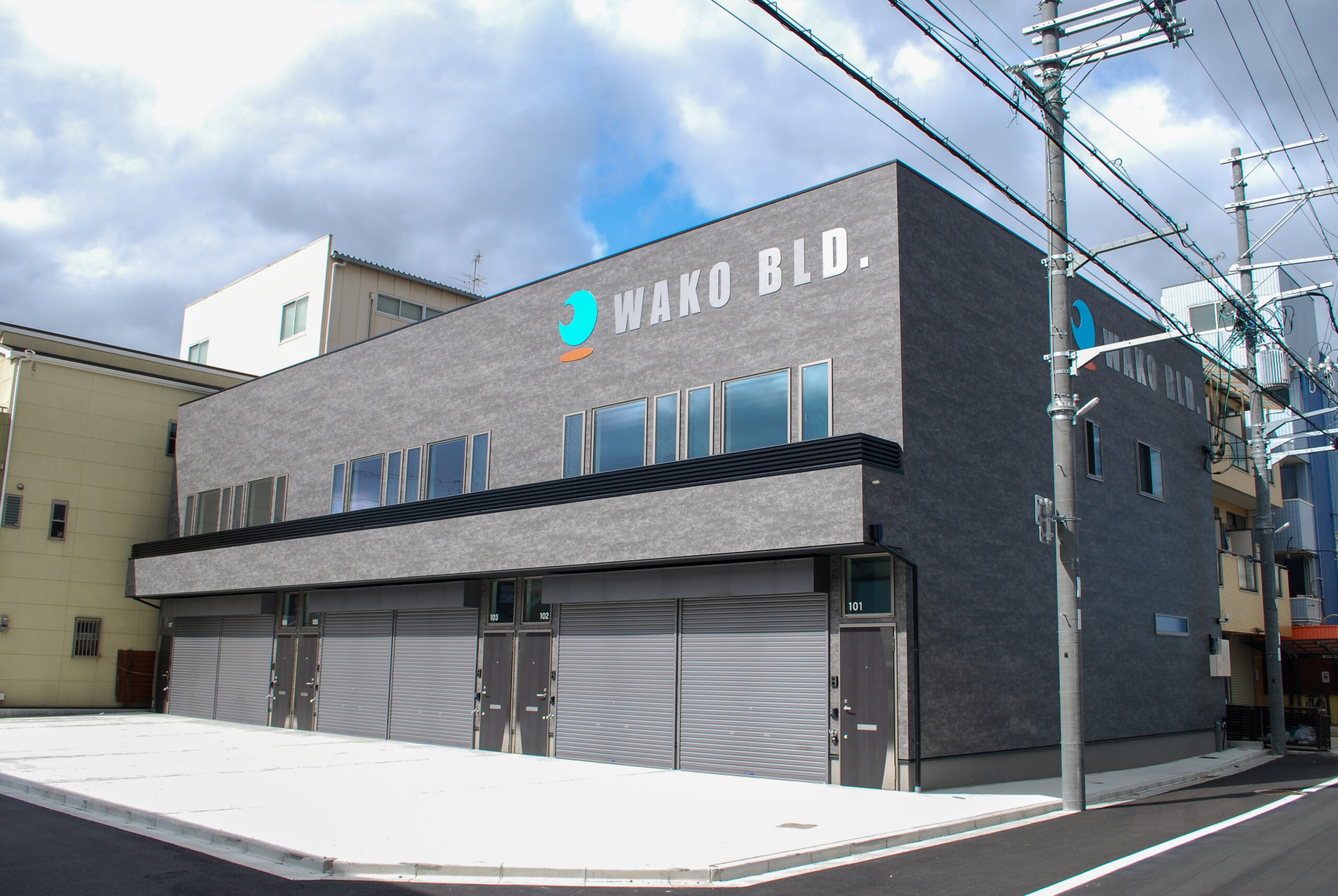 東大阪市高井田中に建つ木造2階建ての駐車場付きテナント事務所ビル外観。外壁にKMEWフィエルテを採用し、倉庫と事務所を併設した施工事例。