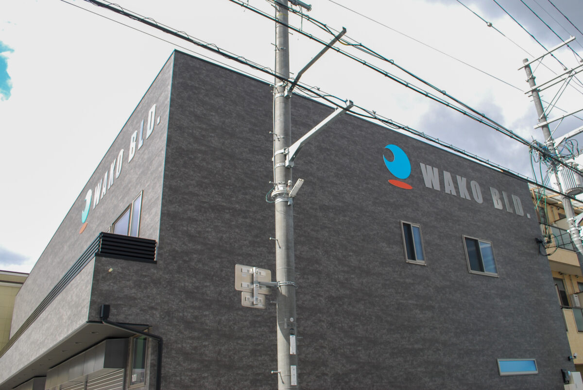 東大阪市高井田中に建つ木造2階建ての駐車場付きテナント事務所ビル外観。外壁にKMEWフィエルテを採用し、倉庫と事務所を併設した施工事例。