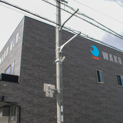 東大阪市高井田中に建つ木造2階建ての駐車場付きテナント事務所ビル外観。外壁にKMEWフィエルテを採用し、倉庫と事務所を併設した施工事例。