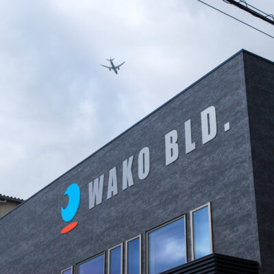 東大阪市高井田中に建つ木造2階建ての駐車場付きテナント事務所ビル外観。外壁にKMEWフィエルテを採用し、倉庫と事務所を併設した施工事例。