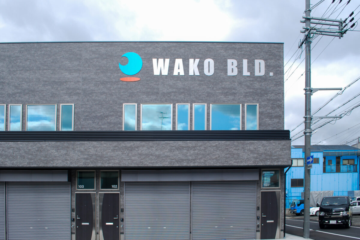 東大阪市高井田中に建つ木造2階建ての駐車場付きテナント事務所ビル外観。外壁にKMEWフィエルテを採用し、倉庫と事務所を併設した施工事例。