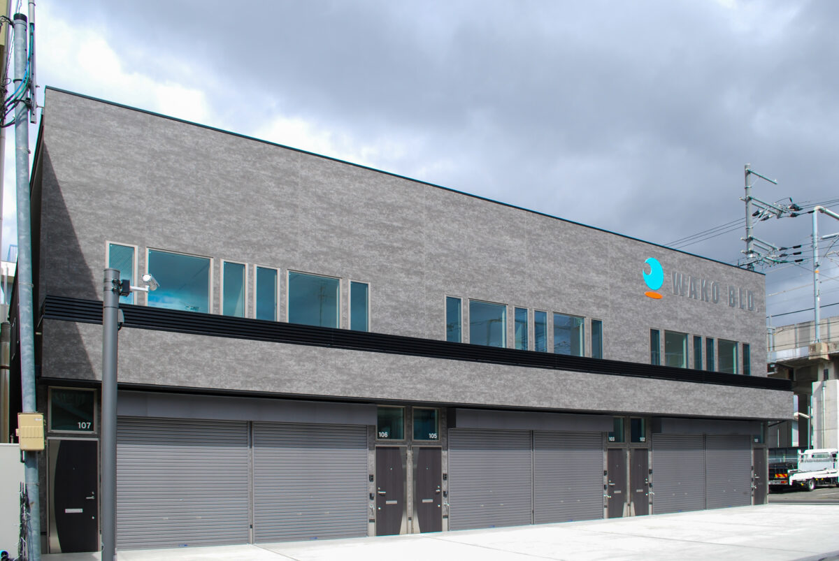 東大阪市高井田中に建つ木造2階建ての駐車場付きテナント事務所ビル外観。外壁にKMEWフィエルテを採用し、倉庫と事務所を併設した施工事例。