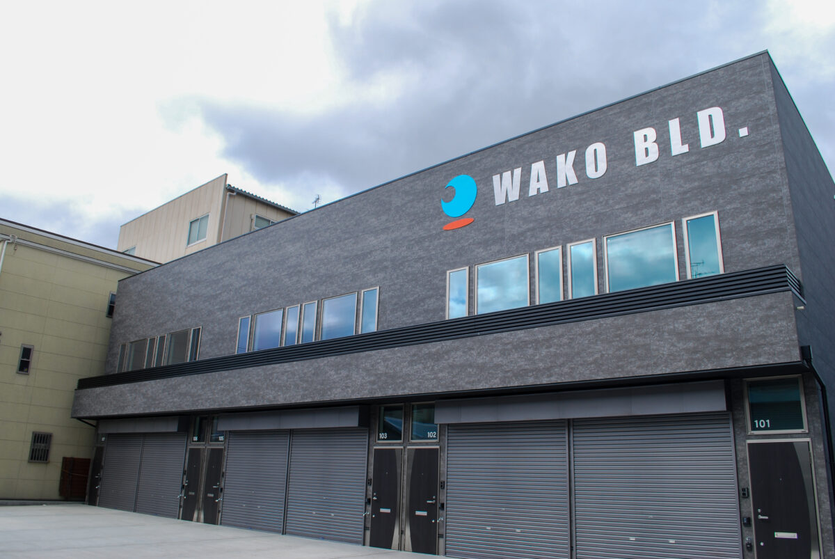 東大阪市高井田中に建つ木造2階建ての駐車場付きテナント事務所ビル外観。外壁にKMEWフィエルテを採用し、倉庫と事務所を併設した施工事例。