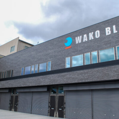 東大阪市高井田中に建つ木造2階建ての駐車場付きテナント事務所ビル外観。外壁にKMEWフィエルテを採用し、倉庫と事務所を併設した施工事例。